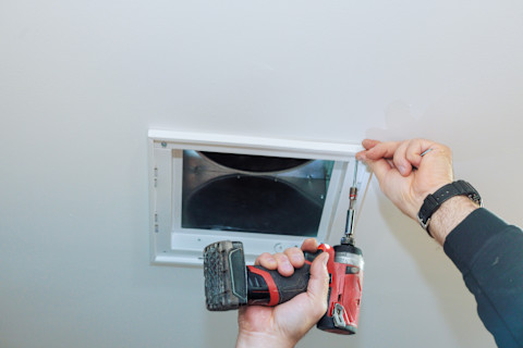 A worker uses a drill to secure a ceiling vent during installation.