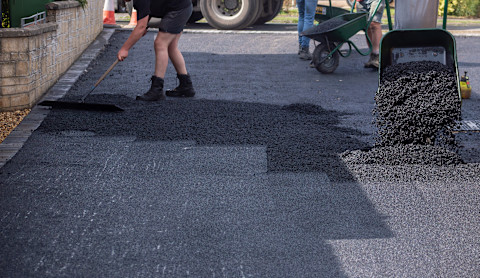 Workers repaving a residential driveway with fresh asphalt using shovels and a wheelbarrow.