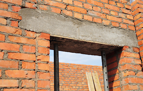 This image shows a steel beam lintel installed in a renovated old house, providing structural support above a doorway. The beam is integrated into exposed brickwork.