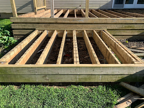 This image shows decking in the construction or deconstruction process. The frame is in place but the boards are missing. The decking frame is on top of soil.