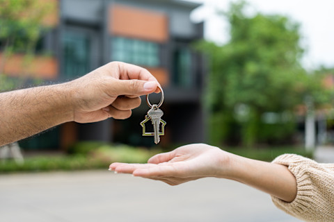Woman buying a new home, holding the key in front of her new house.
