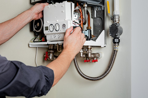 A male plumber's hands taking off the front panel of a boiler in need of service to provide repairs.