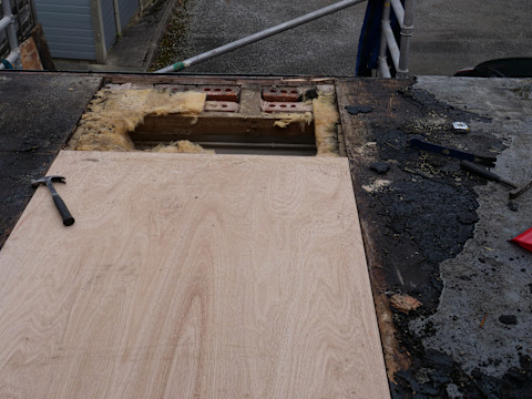 Flat roof renovation working scene, removing old plywood and replacing with new boards.