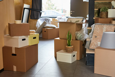 This image shows a hallway of a new home filled with moving boxes and wrapped furniture, ready for unpacking after a relocation.