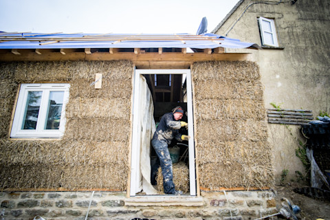 A builder building a straw bale house with white windows.
