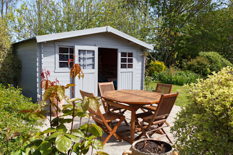 A shed in a garden with a table and chairs in front