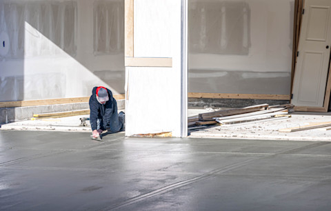 A groundworker wearing a jacket and a cap laying a foundation of a building.