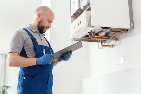 This image shows a gas engineer checking a clipboard while inspecting a gas boiler