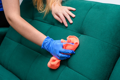 this image shows a cleaner wearing rubber gloves and using a cloth to clean a stain on a green sofa