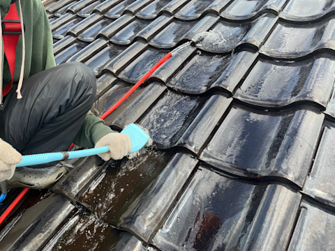 This image shows a tradesperson using a scrubbing brush and a hose to clean roof tiles.
