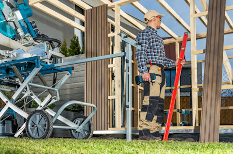 Worker assembling a garden shed on a backyard lawn.