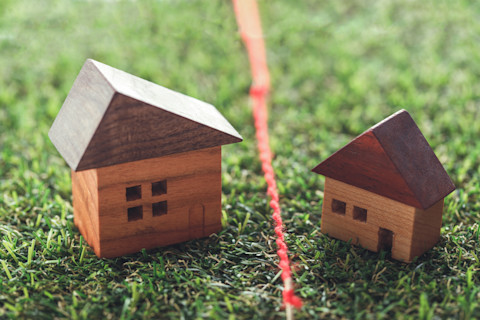 Two small model homes made of wood are placed on artificial grass, with a red rope separating them