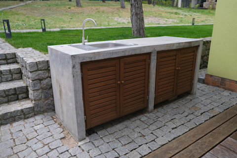 A modern outdoor kitchen sink unit with a stainless steel sink, faucet, and countertop, set in a stylish outdoor cooking area with cabinets.