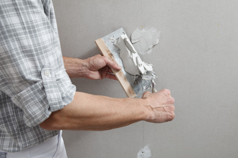 Plasterer putting stucco on plasterboard wall using a trowel and a spatula