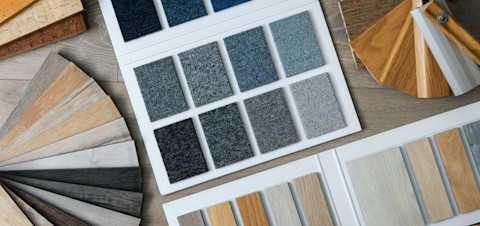 A collection of flooring material and skirting samples, including carpet and laminate arranged on a wooden surface. The samples showcase various textures and colours, providing options for interior design and flooring selection.