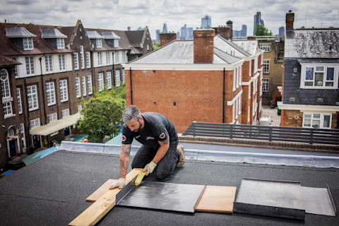 A roofer working on the roof of a house and fixing a rubber roof.