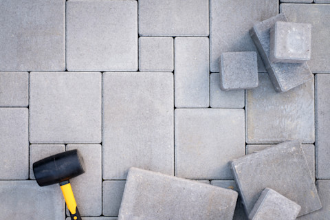 This image shows patio paving stones being installed with a rubber mallet in the bottom left corner.