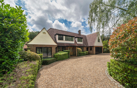 Large detached house with gravel drive and shrubs on summer day.