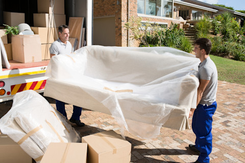 This image shows two removal men carrying a sofa covered in protective plastic to or from a removals lorry.