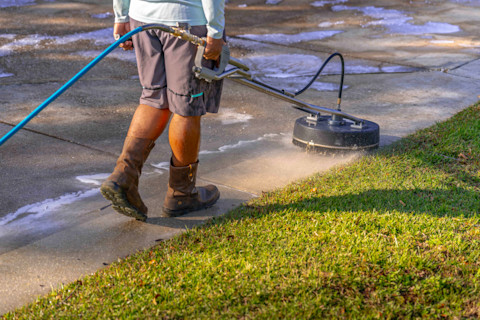A tradesperson is using a power washer to clean a concrete driveway.