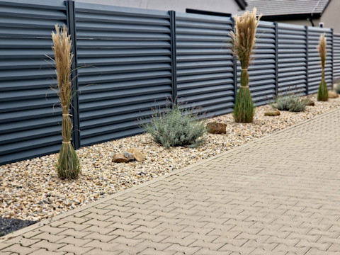 Black privacy fence panels bordering a garden, placed behind a gravel pathway with plants on top.