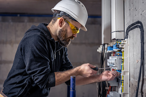 An electrician installing modern circuit breakers to replace an old fuse box, showcasing the wiring and components of the electrical panel during the upgrade process.