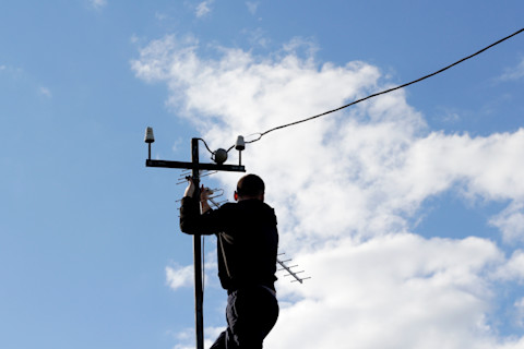 A tradesperson is safely installing a new TV aerial on a roof.