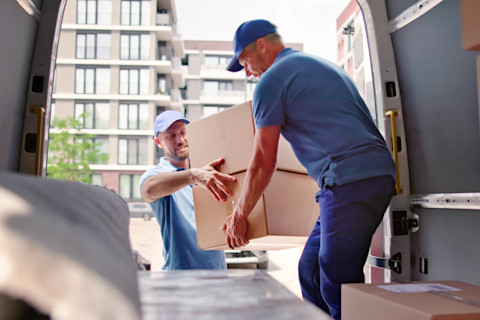 This image shows two removal men passing a cardboard box to be put in the back of a van, suggesting a house move.