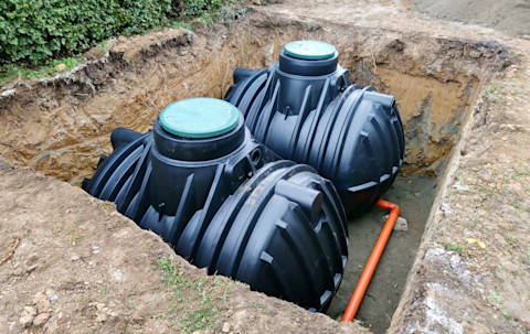Close-up of a rainwater harvesting system. The image shows large storage tanks connected to gutters and downspouts, with rainwater being collected and directed into the tanks.