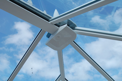 Upward view of blue sky through a modern conservatory's glass roof structure.