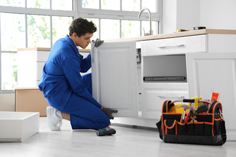 A tradesman is fitting a new kitchen cabinet in a home.