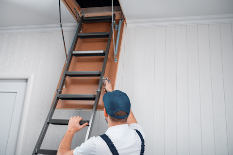 A man is installing a new loft ladder into a loft hatch space.