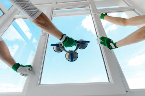 Four hands are holding glass of a new window for proper installation.