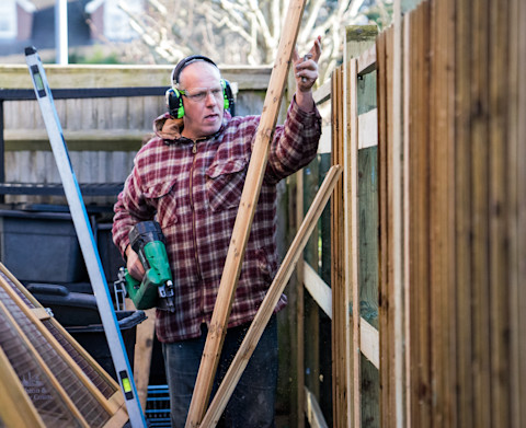 This image shows a fencer installing a fence in a garden