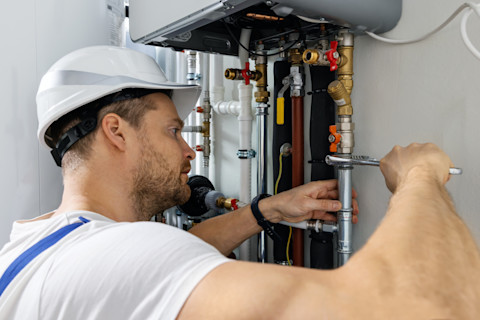 A technician replacing a gas pipe in a home's plumbing system, with new pipe sections being installed and tools laid out nearby.