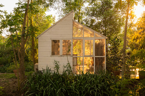 A light and airy furnished sun room in an English country style garden, in the evening, with the setting sun in the background.