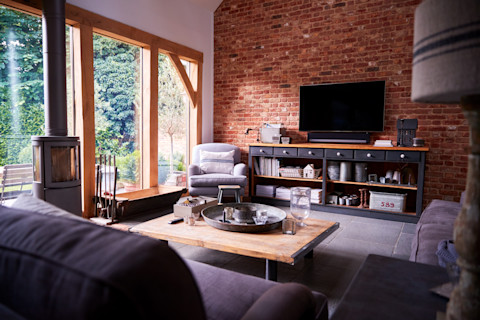 Cosy living room with an exposed brick wall, large windows, and a wood-burning stove.